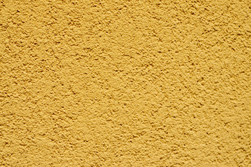 A fragment of the wall of the house. Plaster of heat-yellow sand color. Granulated surface