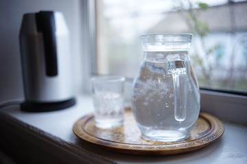 Jug of water and a glass in a tray on the windowsill.