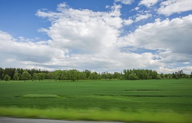 Beautiful view of landscape with green fields, green forest trees and blue sky with white clouds. Gorgeous backgrounds.