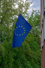 Blue flag with twelve yellow stars in the wind against blue sky and green trees foliage