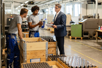 Two metal workers cooperating with quality control inspector in industrial facility.