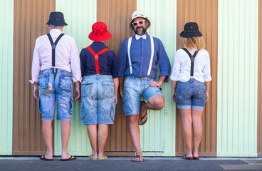 Adult group of people standing in front of colorful wall.Two women and two men posing for funny photo with suspenders and bow tie. Caucasian persons.