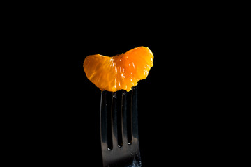 Mandarin pierced on a fork isolated on a black background