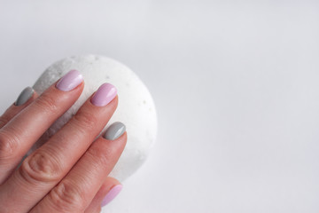 The hand with pastel color manicure hold white salt ball for bath on grey background. Space for text