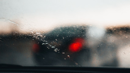 Abstract car window in raining day. View from car seat. Blur Background at sunset. Drops of rain on car window pane. Blurred droplet on car window, sun light over empty road. Driving in rain weather.