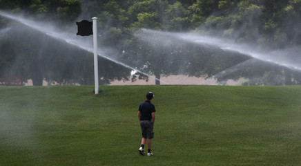 A junior golfer cools off by standing in the mist of a golf course sprinkling system