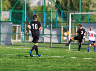 Boys in white and black sportswear plays  football on field, dribbles ball. Young soccer players with ball on green grass. Training, football, active lifestyle for kids concept 