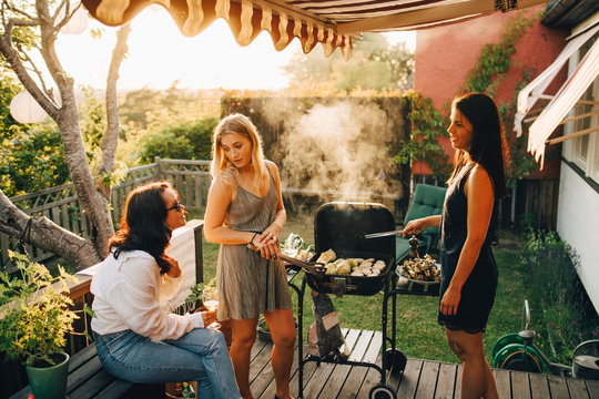 Friends talking while grilling food on barbecue for dinner party in yard