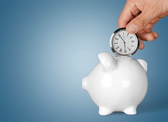 Hand depositing  clock  in piggy bank on background