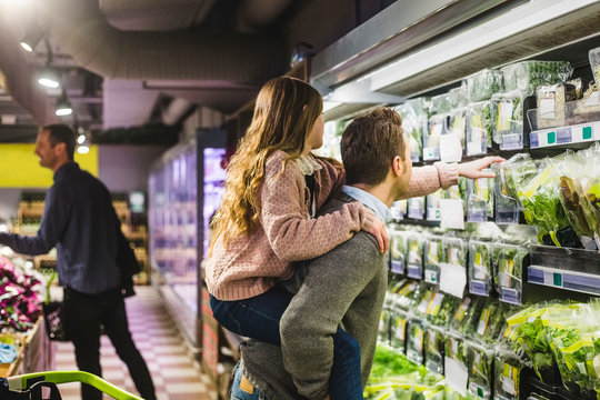 Side view of daughter picking up vegetable packet while being piggybacked by father in store