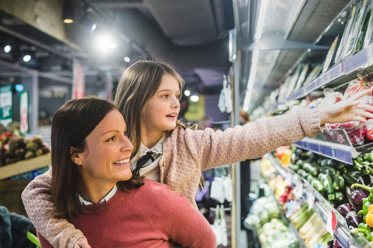 Smiling mother piggybacking daughter while grocery shopping in supermarket