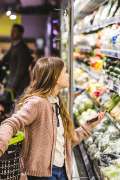 Side view of girl looking at vegetables on shelves in store