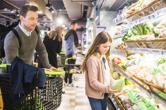 Father looking at cute daughter choosing vegetable in supermarket