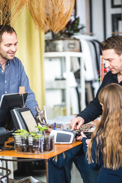 Girl typing pin code at checkout counter in clothing store by father