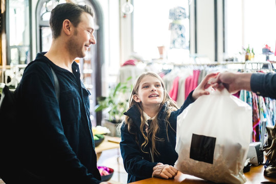Cute daughter receiving shopping bag from cashier by father at checkout counter