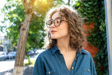 Outdoor close up portrait of young beautiful stylish happy smiling curly girl wearing sunglasses,...