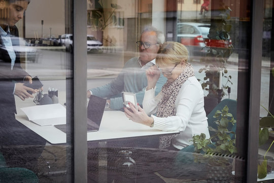 Senior couple looking at smart phone while sitting in real estate office
