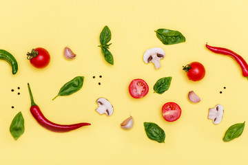 Various fresh vegetables and herbs on yellow background.