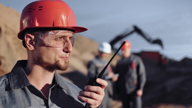 Confident male foreman worker discussing using walkie talkie in construction site at sunset
