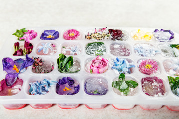 Tray with Frozen Flowers in Ice Cubes on grey Background, top view, copy space for text