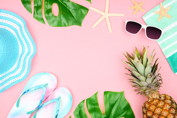 Beach accessories on a pink background. Summer vacation concept frame with copy space. Sunglasses, sea shells, towel, flip flops, palm leaves, blue striped hat and pineapple.
