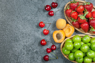 Summer fruits, green plum, red cherry, strawberry, apricot on grey rustic table. top view, copy space for text, selective focus