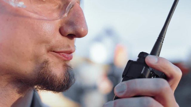 Extreme close-up mouth of bearded male construction worker talking using walkie talkie side view