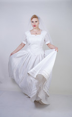 Fototapeta na wymiar pretty curvy adult woman with short hair wearing long vintage wedding dress with sun style skirt. young caucasian bride with veil on white studio background alone.