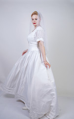 Fototapeta na wymiar pretty curvy adult woman with short hair wearing long vintage wedding dress with sun style skirt. young caucasian bride with veil on white studio background alone.