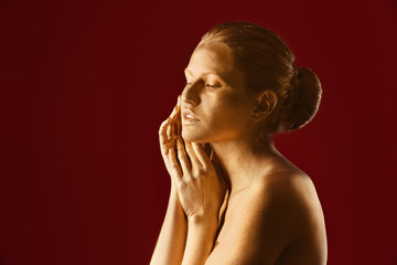Portrait of beautiful lady with gold paint on skin against color background