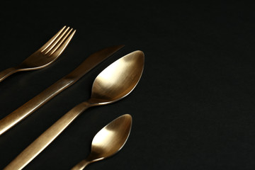 Set of gold cutlery on black background. Space for text