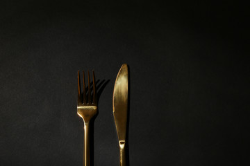 Gold fork and knife on black background, top view. Space for text