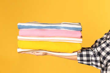 Young woman holding clean laundry on color background, closeup