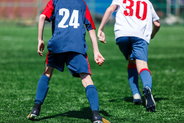 Boys at blue white sportswear run, dribble, attack on football field. Young soccer players with ball on green grass. Training, football, active lifestyle for kids