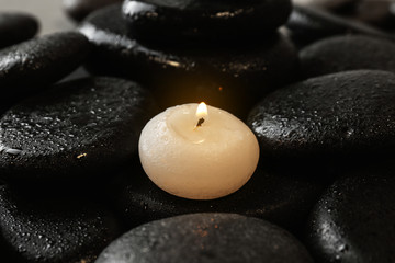 Fototapeta na wymiar Small burning candle on beautiful wet spa stones