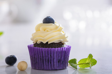 Cupcake with blueberry and hazelnut in purple wrap on white natural marble surface.