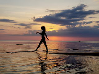 silhouette of a girl walking on the beach sand. Shooting against the sun. Sunset over the sea