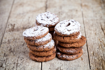 Fresh baked chocolate chip cookies with sugar powder stacks on wooden table.