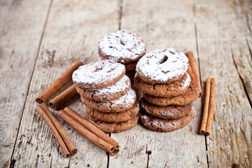 Fresh baked chocolate chip cookies with sugar powder and cinnamon sticks on wooden table.