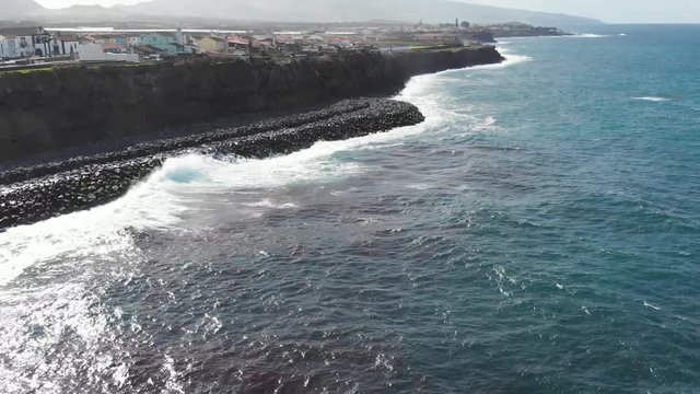 Aerial Drone Azores Portugal waves crashing on the beach tilt up from ocean to cliff village and mountains