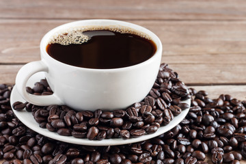 Coffee is hot, dark in a white coffee cup, placed on an old wooden table and has coffee beans - picture