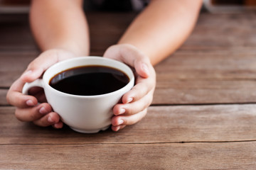 Woman hand holding a cup of coffee on an old wooden table - photo