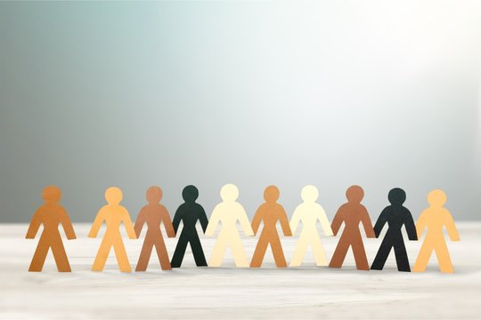 Row of paper people holding hands on table on light background