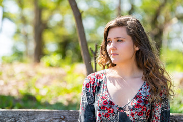 Fototapeta premium Woman closeup portrait of face sitting on a wooden bench in sunny forest during spring in Mill Mountain park in Roanoke, Virginia