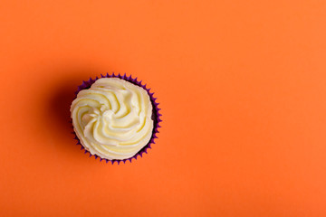 Cupcake in purple wrap on coral colour background. Minimal. Top view with copy space.