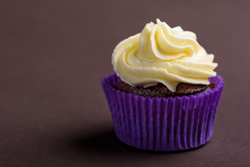 Cupcake in purple wrap on dark brown background. Minimalist. Сopy space.