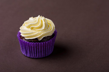 Cupcake in purple wrap on dark brown background. Minimalist. Сopy space.