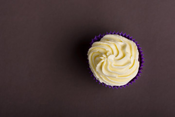 Cupcake in purple wrap on dark brown background. Minimal. Top view with copy space.