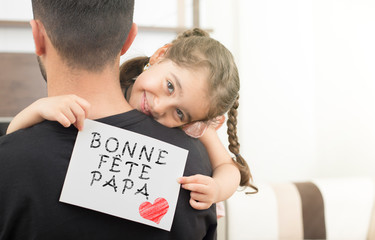 little girl hugging her father and showing the message of congratulation.with french text