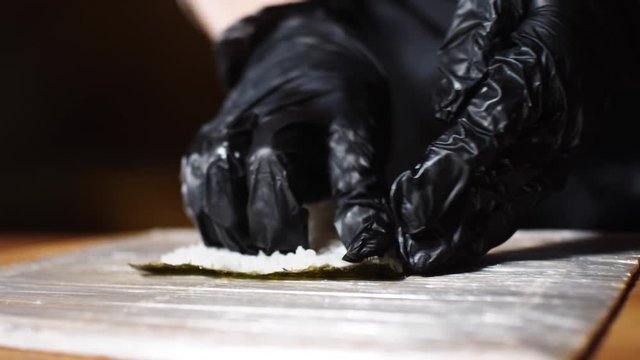 Close-up of Sushi Master's hands in black gloves making tasty sushi and rolls with bamboo mat. Frame. Traditional Japanese food